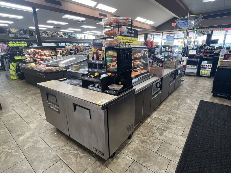 Convenience store foodservice area featuring grab-and-go foods, hot food merchandising, condiment station, and customer-focused product displays designed to improve visibility and purchasing convenience.